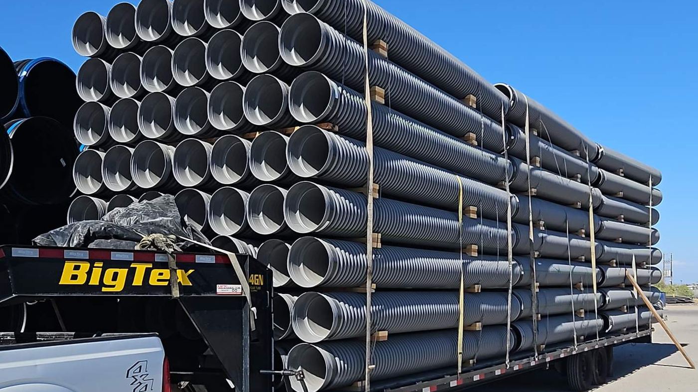 Large-diameter corrugated pipe stacked and strapped on a gooseneck flatbed